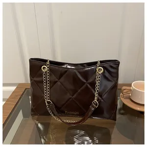 Détail d'un sac cabas marron matelassé avec chaîne dorée et texture cuir brillant