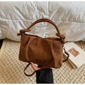 Close-up of brown suede handbag with vertical pleats and stylish knotted handle
