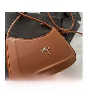 Close-up of brown leather handbag featuring a silver metal bow and textured material