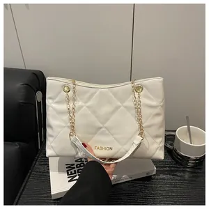 Détail du sac cabas matelassé blanc avec chaîne dorée sur une table noire