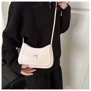 Close-up of off-white faux leather hobo bag with a decorative metal bow and fine stitching