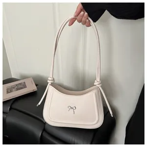 Detail of cream shoulder bag with silver metal bow and knotted leather strap