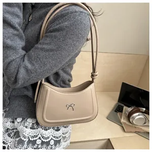 Detail of a khaki crescent shoulder bag with a metal bow accent and slim knotted straps