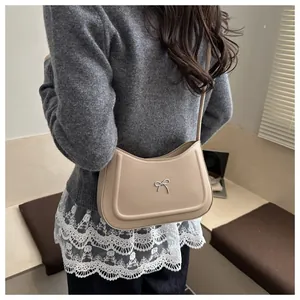Chic beige hobo bag with silver bow detail worn with casual outfit on shoulder