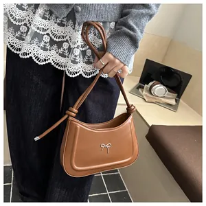 Detail of a brown shoulder bag featuring a silver metal bow and adjustable strap