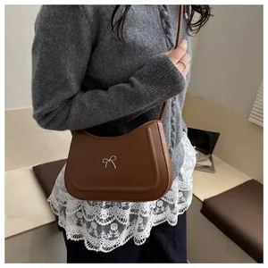 Brown semi-circle shoulder bag with silver bow detail shown on model in casual outfit