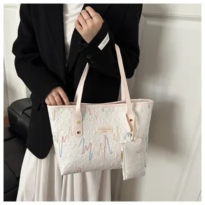 Close-up of white pleated tote bag featuring colorful embroidery and small pouch charm