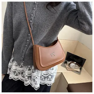 Brown half-moon shoulder bag with silver bow detail shown in a casual lifestyle setting
