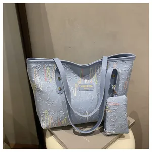 Detail of light blue tote bag set with wavy embroidery and metal rivet hardware