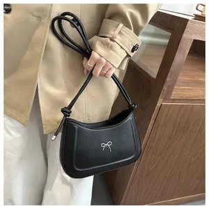 Detail of a black shoulder bag featuring a silver bow accent and slim rounded straps
