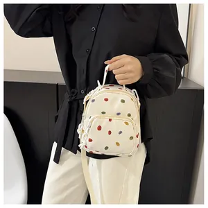 Dettaglio di un mini zaino in tela bianca con pois colorati e tracolla regolabile bianca