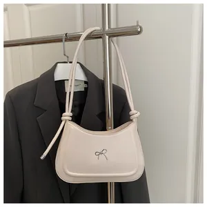 Detail of minimalist beige underarm bag with silver bow hardware and knotted shoulder strap