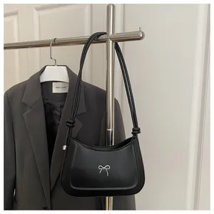 Detail of black leather shoulder bag featuring a silver metal bow and slim knotted strap