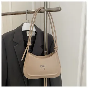 Detail of beige faux leather shoulder bag with silver bow accent and knot strap
