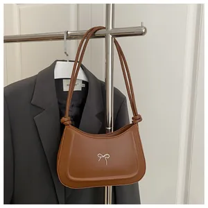 Detail of a brown leather crescent shoulder bag featuring a silver metal bow accent