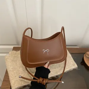 Minimalist caramel brown leather shoulder bag with a silver metal bow accent