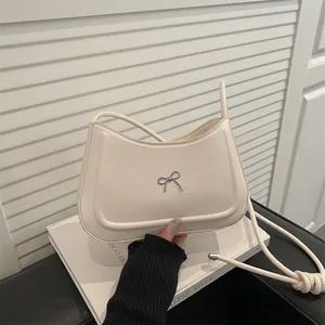 Minimalist cream shoulder bag with silver bow detail and thin round strap on white books