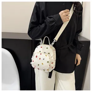 Dettaglio di un mini zaino in tela crema a pois colorati indossato come borsa a tracolla