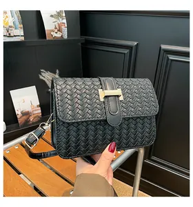 Detailed close-up of black woven leather texture and gold buckle on a square crossbody bag