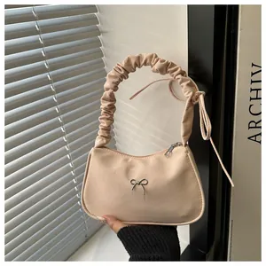 Detalle del bolso beige con mariposa de metal plateado y asa con diseño fruncido