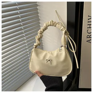 Detalle del bolso crema con asa fruncida y adorno de mariposa plateada