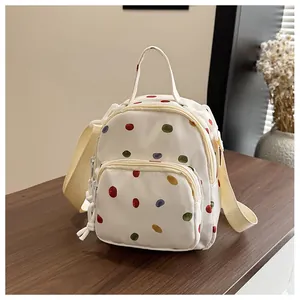 Dettaglio mini zaino in tela beige con pois colorati su una superficie in legno