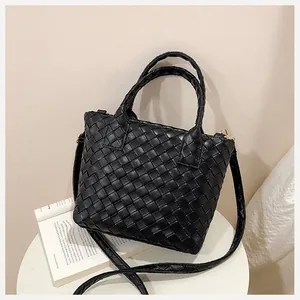 Detailed view of black woven texture handbag with golden hardware on a white table