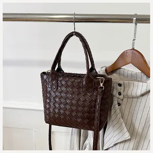 Detail of dark brown woven handbag with gold hardware hanging on a metal rack