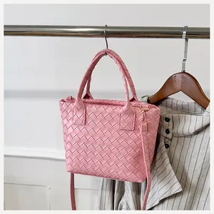 Detail of pink woven tote bag showing leather texture and gold zipper closure