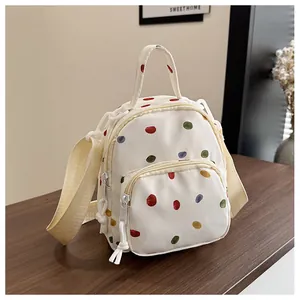 Dettaglio dello zainetto in tela bianca con pois colorati su un tavolo di legno scuro