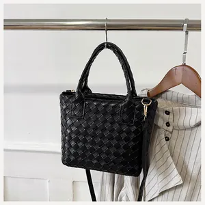 Close-up of black woven leather handbag with gold hardware and adjustable strap