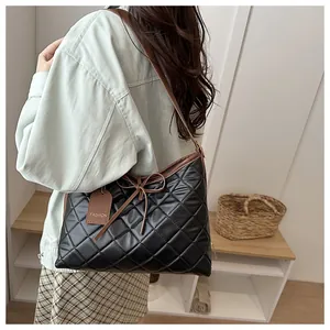 Detail of black quilted tote bag with brown trim and bow, shown on a model