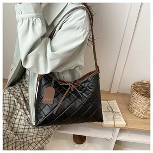 Detail of black quilted tote bag with brown leather straps and bow on a soft background