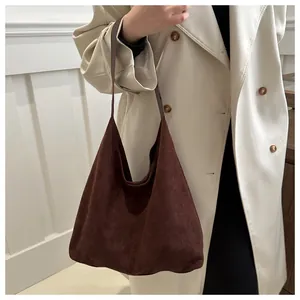 Detail of a dark coffee brown suede hobo bag with slim straps worn by a model in soft light
