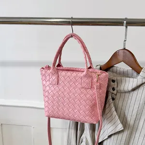 Pink woven leather tote bag with dual handles and crossbody strap on minimalist hanger