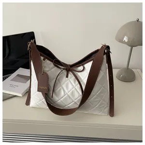Detail of white quilted tote bag with brown leather straps and fashion tag on desk