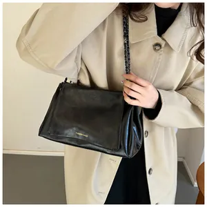 Detail einer schwarzen Kunstledertasche mit Goldbeschriftung und Metallkettenriemen