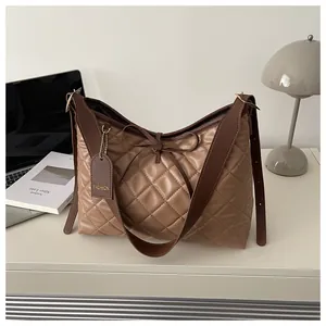 Close-up of brown quilted tote bag with bow detail and fashion tag on white desk