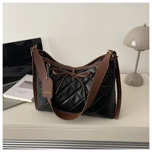 Close-up of black quilted tote bag with brown shoulder strap and bow detail on a desk