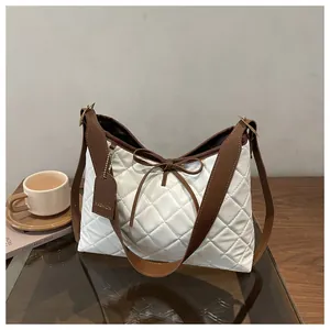 Detail of white quilted tote with brown leather straps and a delicate bow decoration