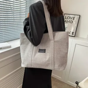 Detail of grey canvas tote bag with black patch shown on a shoulder in a modern room