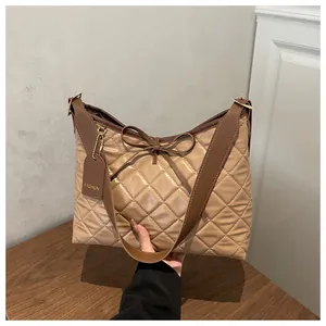 Detail of quilted tote bag with bow accent and brown leather strap on wooden desk