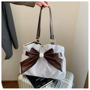 Detail of white polka dot tote bag with a large brown leather bow and delicate lace trim