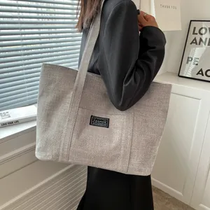 Detail view of a gray fabric tote bag with a fashion label and wide shoulder strap
