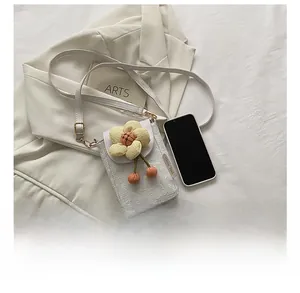 Mini white crossbody bag with floral texture and fabric flower next to a phone for scale