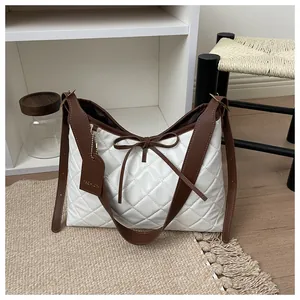 Detail of white quilted hobo bag featuring brown bow and fashion tag on hobo purse