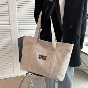 Beige canvas tote bag with fashion patch and wide shoulder straps shown on a model