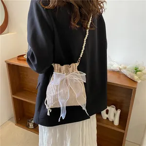 Detail of beige pleated bucket bag with large organza bow and elegant pearl strap