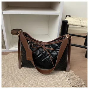 Detail of black quilted leather tote bag with brown strap and bow charm on a carpet