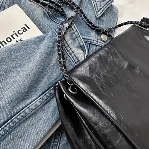 Retro schwarze Kette Umhängetasche aus Leder mit Falten-Textur auf Denim-Hintergrund